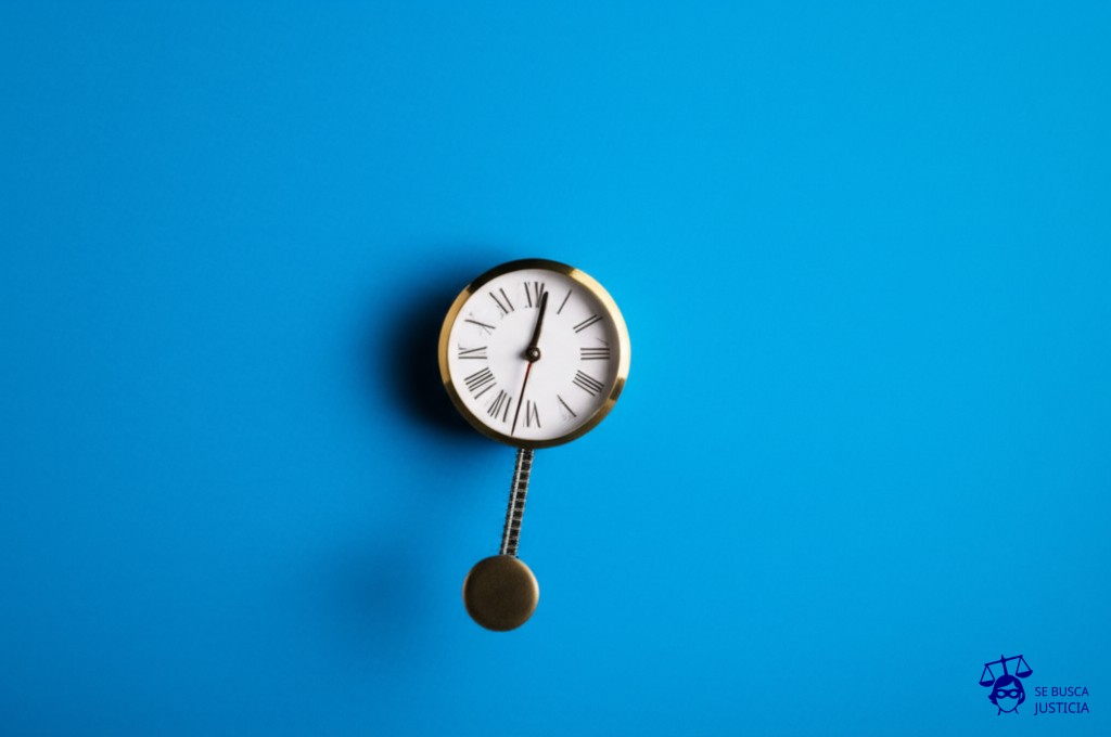 Un reloj de péndulo con el péndulo hecho de vías de tren, oscilando directamente hacia un agujero en la pared. Representa: Accidente en vía férrea sin barreras