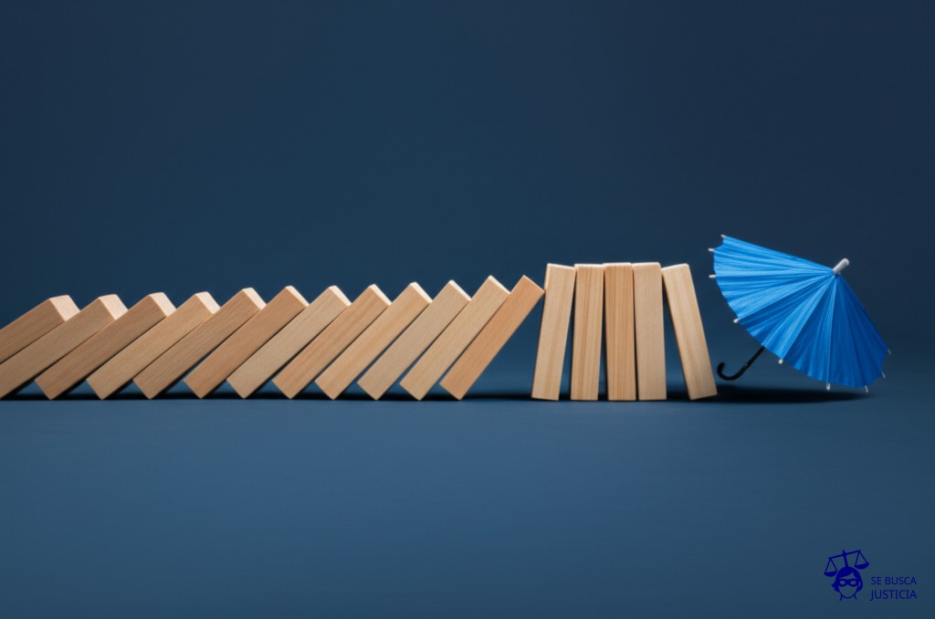 Un dominó gigante, con muchas fichas, todas cayendo en cascada. La última ficha, al caer, golpea un pequeño paraguas que se pliega instantáneamente. Representa: Cobertura limitada o nula en caso de siniestros múltiples