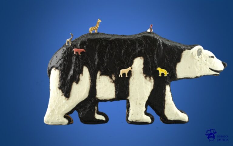 Un gran pastel con forma de oso polar, decorado con glaseado de petróleo derramado y adornado con pequeñas figuritas de animales ahogándose en el glaseado. Representa: Delitos ambientales con daños a la fauna
