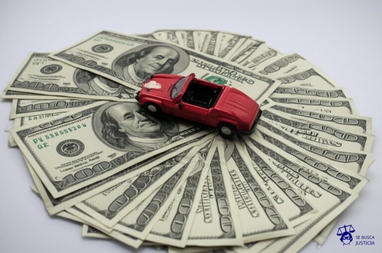 Un montón de billetes de banco desparramados, con un coche de juguete destrozado en medio. Representa: Fallecido sin testamento en accidente