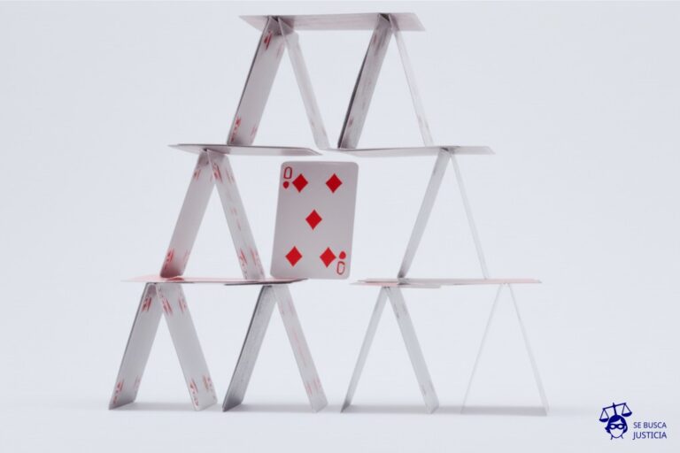 Un gran castillo de naipes, con un solo naipe (el del centro) fuera de lugar, ligeramente inclinado y a punto de caer. Representa: Incumplimiento de normas del Banco Central