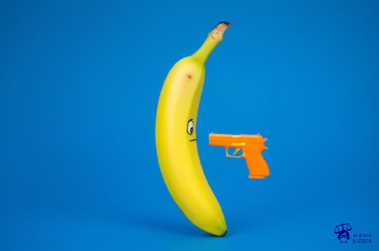 Un plátano, con una pistola de juguete apuntándole. Representa: Robo con violencia e intimidación