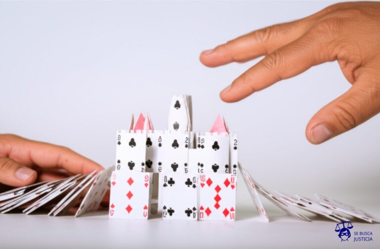 Un delicado castillo de naipes (representando el matrimonio) a punto de derrumbarse, sostenido precariamente por una sola mano temblorosa (la persona vulnerable), mientras que una mano gigante y robusta (el otro cónyuge) se acerca amenazante. Representa: Solicitud de divorcio por parte de un cónyuge en situación de vulnerabilidad o víctima de violencia, que requiere protección especial y medidas urgentes durante el proceso de disolución matrimonial.