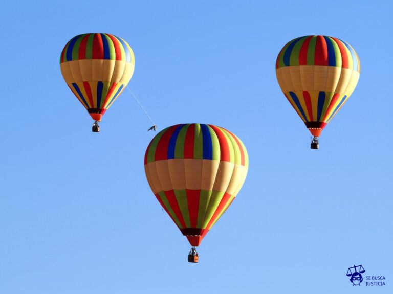 Un grupo de globos aerostáticos (ciclistas) en plena carrera, uno de ellos (Armstrong) siendo cortado por la cuerda que lo sostenía, cayendo rápidamente. Representa: Suspensión de por vida de Lance Armstrong por dopaje (Ciclismo)