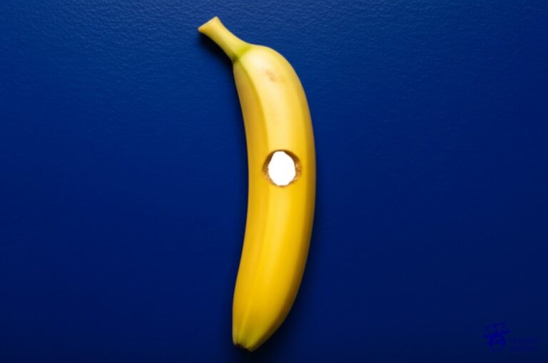 Un plátano pegado con cinta adhesiva a una pared de galería, con un pequeño agujero en el centro, revelando un lienzo blanco detrás. Representa: Venta de imitaciones de obras de arte protegidas en galerías