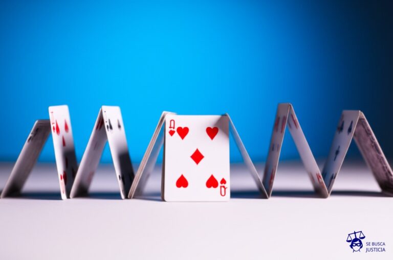 Un castillo de naipes a punto de colapsar, con una carta clave (la base) retirada. Representa: Negativa de un Estado a ratificar un tratado de desarme nuclear lo que debilita el régimen de no proliferación y plantea un riesgo para la seguridad global al no someter su programa nuclear a inspecciones internacionales