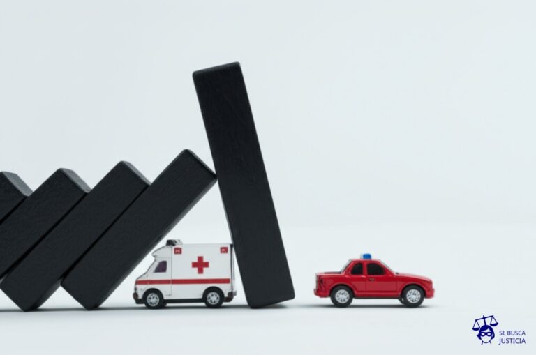 Un dominó gigante, pintado de negro, que se apoya precariamente sobre una fila de autos de juguete. El dominó está a punto de caer, aplastando una ambulancia de juguete que intenta pasar por debajo. Representa: Un grupo de activistas bloquea una autopista principal durante una protesta, generando un caos vehicular de varias horas. El bloqueo impide el paso de una ambulancia que transporta a un paciente en estado crítico, quien fallece. La fiscalía acusa a los líderes de la protesta de coacción agravada y homicidio culposo, pero la defensa invoca el derecho a la protesta social.